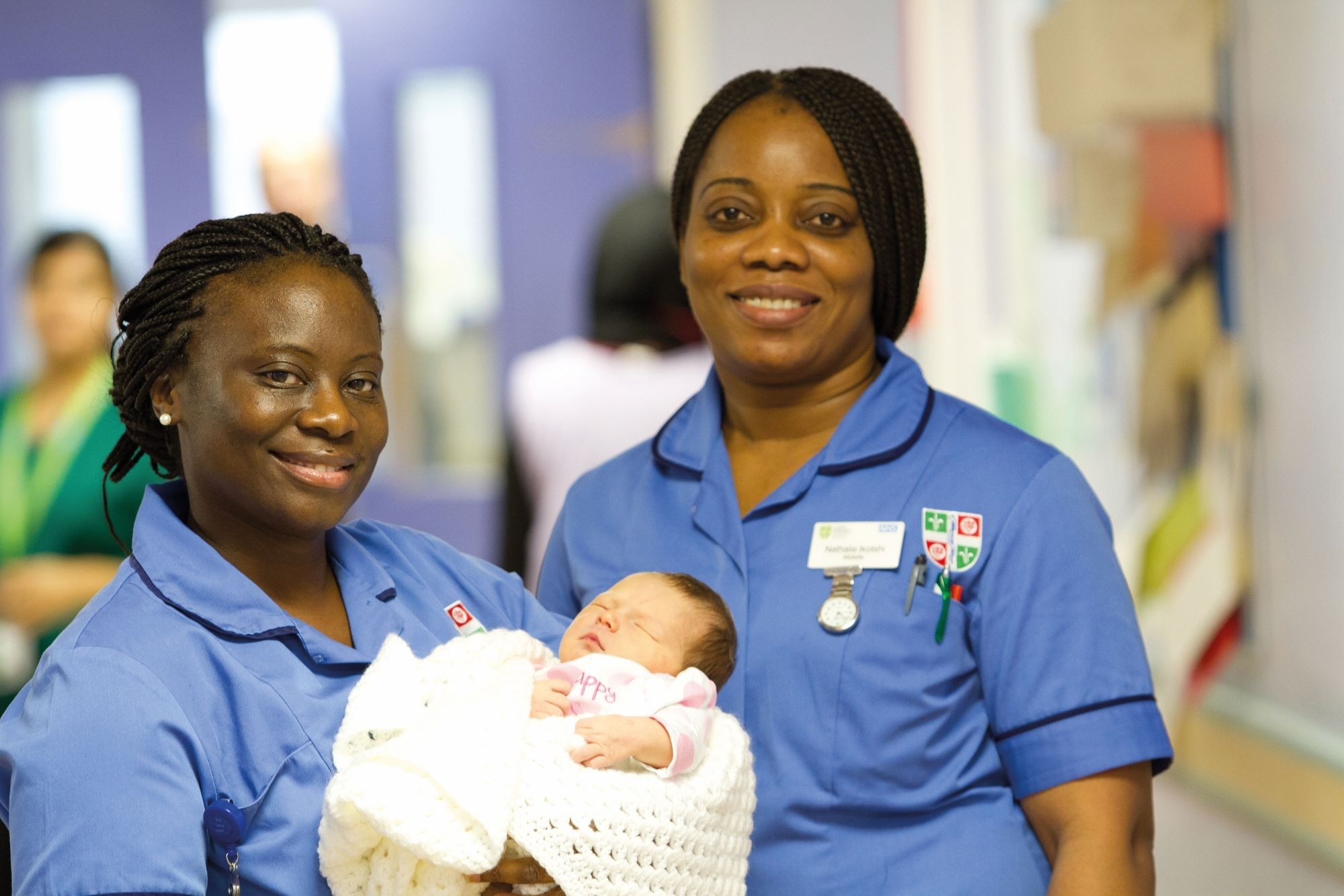 Two smiling nurses hold a baby
