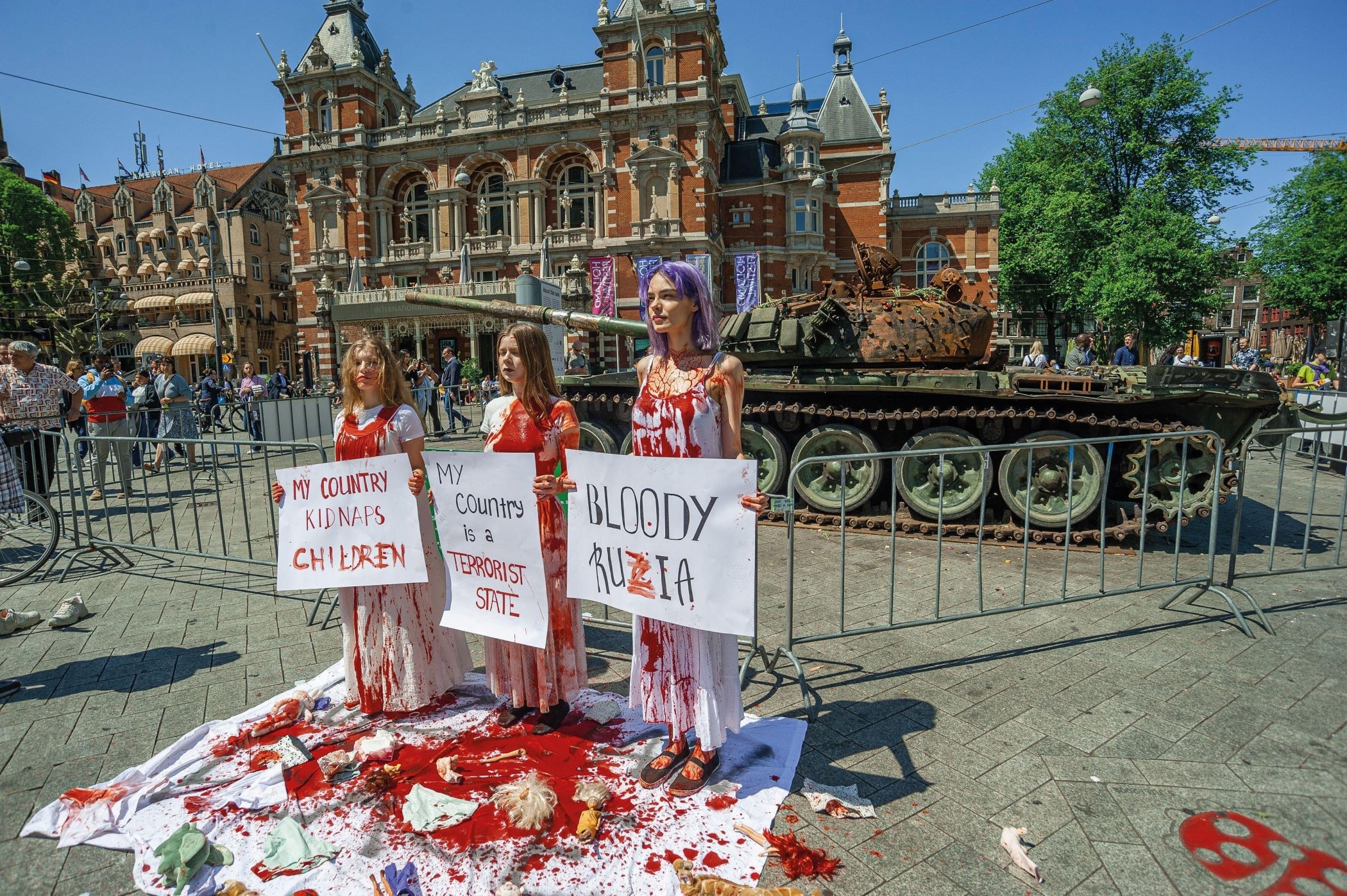 Three women dressed in white and covered in fake blood stand in front of a tank as part of a 2023 protest organised by the Feminist Anti-War Resistance in Amsterdam
