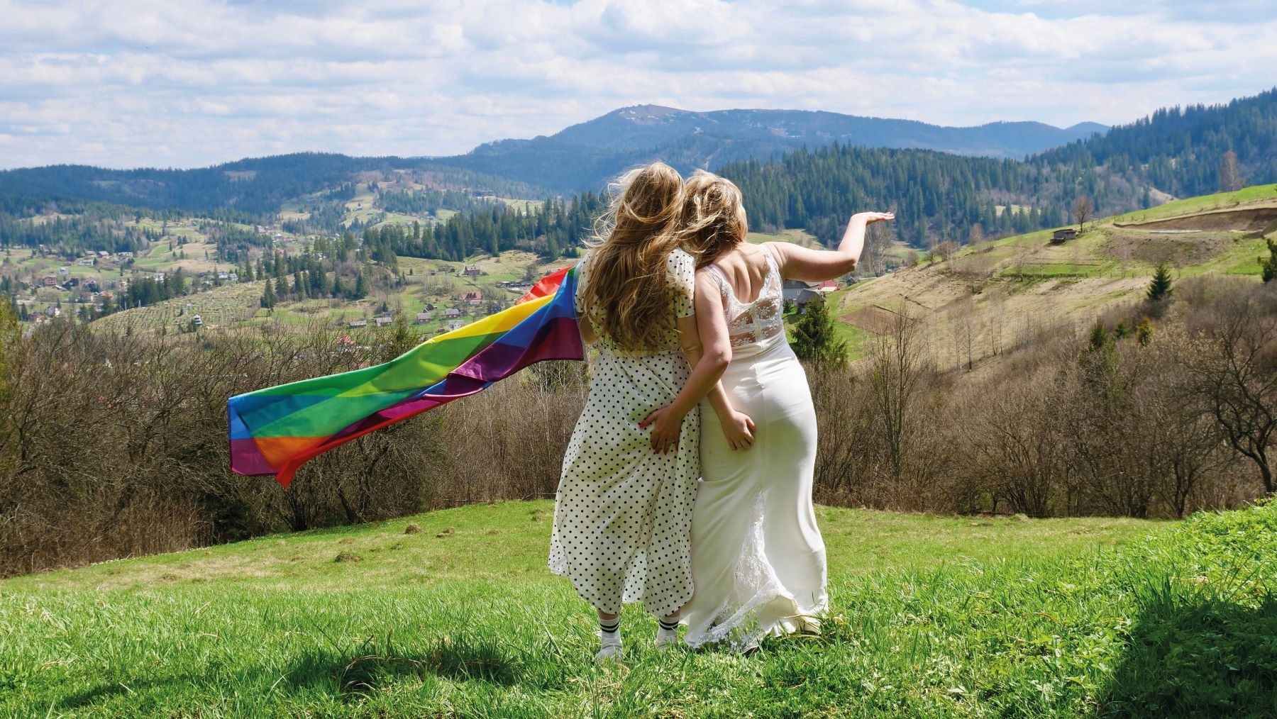 A pair of brides waving the rainbow flag on their wedding day