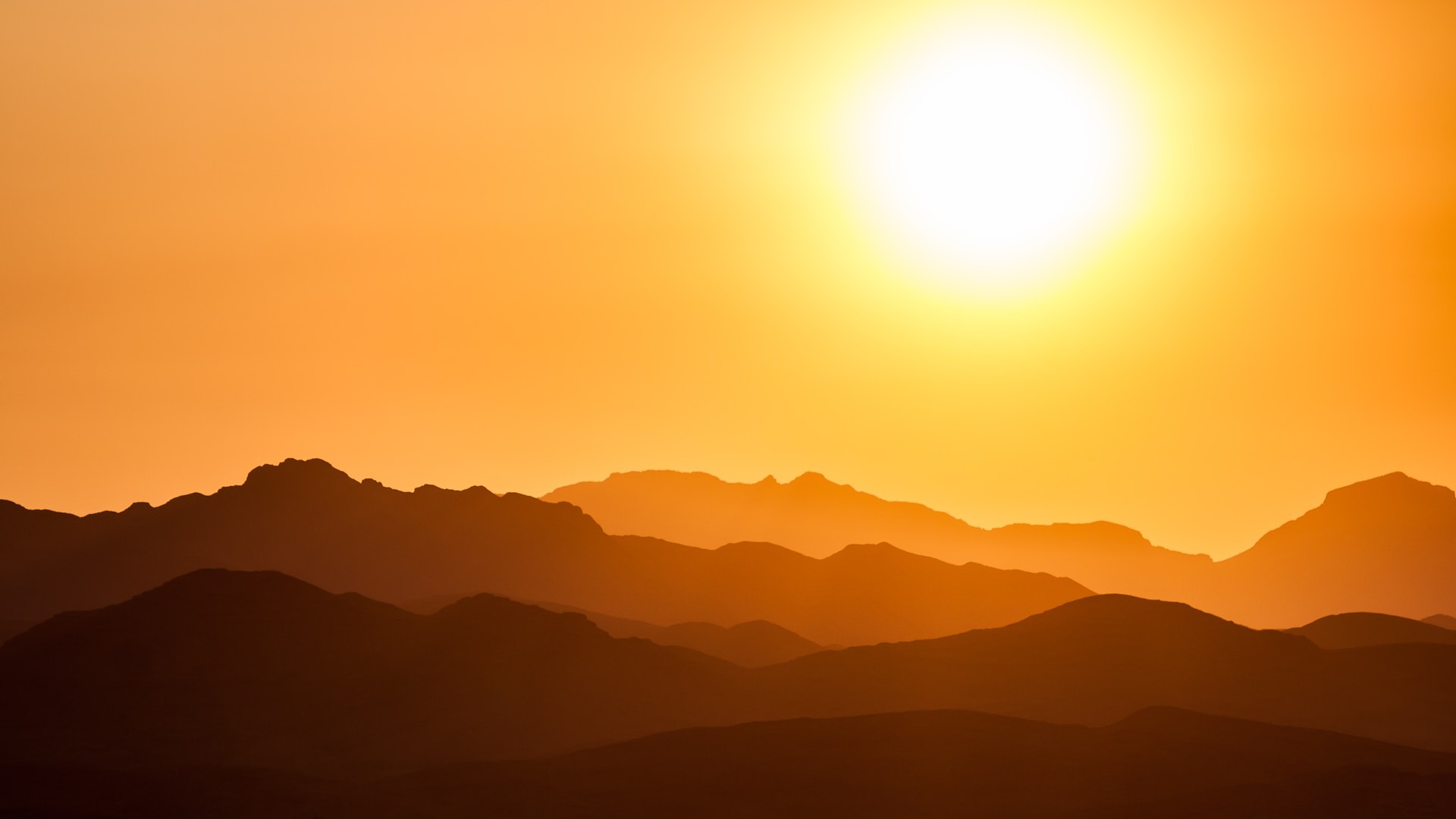 A bright yellow sun rises over mountains in Nevada