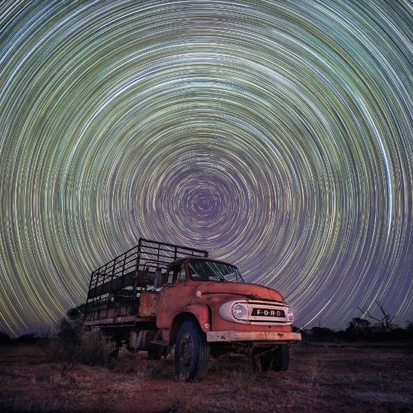 Star trails from the Earth’s rotation, captured using long exposure, appear as a series of tightly-spun glowing circles above a cattle truck in the Western Australian Wheatbelt