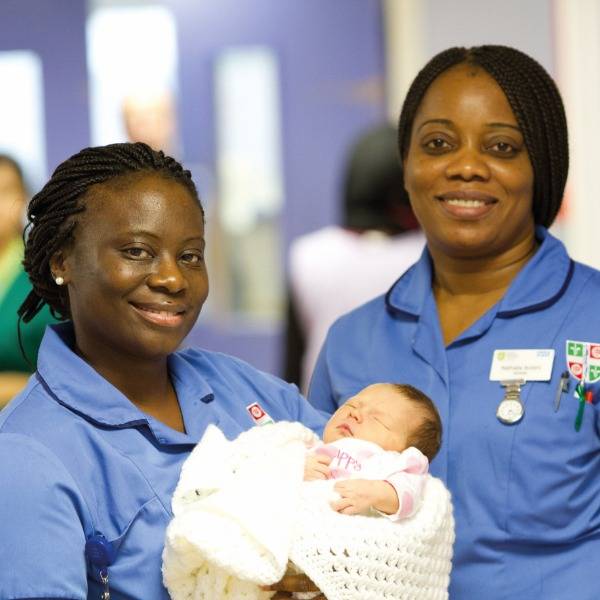 Two smiling nurses hold a baby