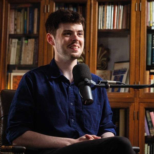 A photo of Alex O'Connor recording a podcast in a room lined with books