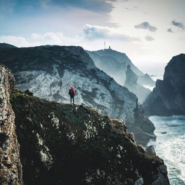 A man stands on a clifftop, surveying the vast sea and landscape in front of him