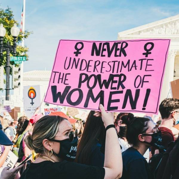 In the middle of a protest in Washington DC, a woman holds a sign reading 'Never underestimate the power of women'