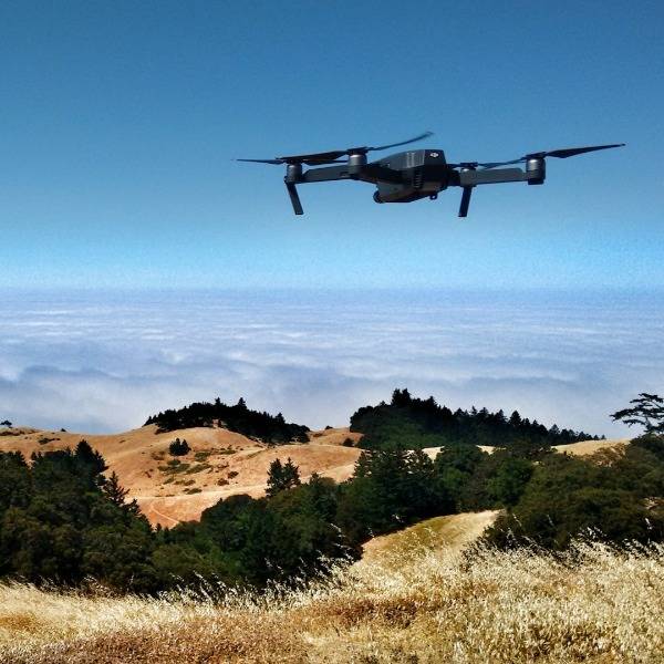 A drone used for photography hovers over a hilly landscape