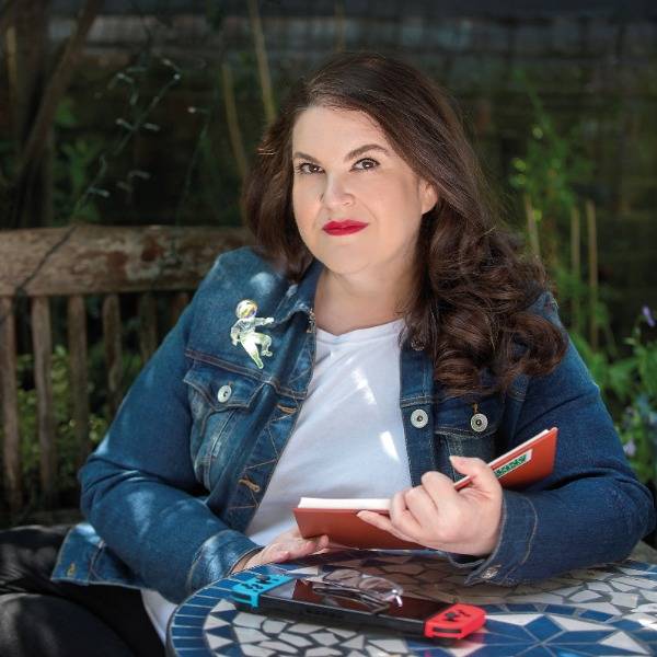 A photo portrait of Naomi Alderman sitting in a garden and reading a book