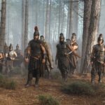 Odysseus and his men, dressed in armour, stand together in a forest