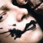 A detail from the film poster of “The Bride!” shows the Bride with black splattered across her face while Frank presses his face against hers
