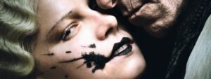 A detail from the film poster of “The Bride!” shows the Bride with black splattered across her face while Frank presses his face against hers