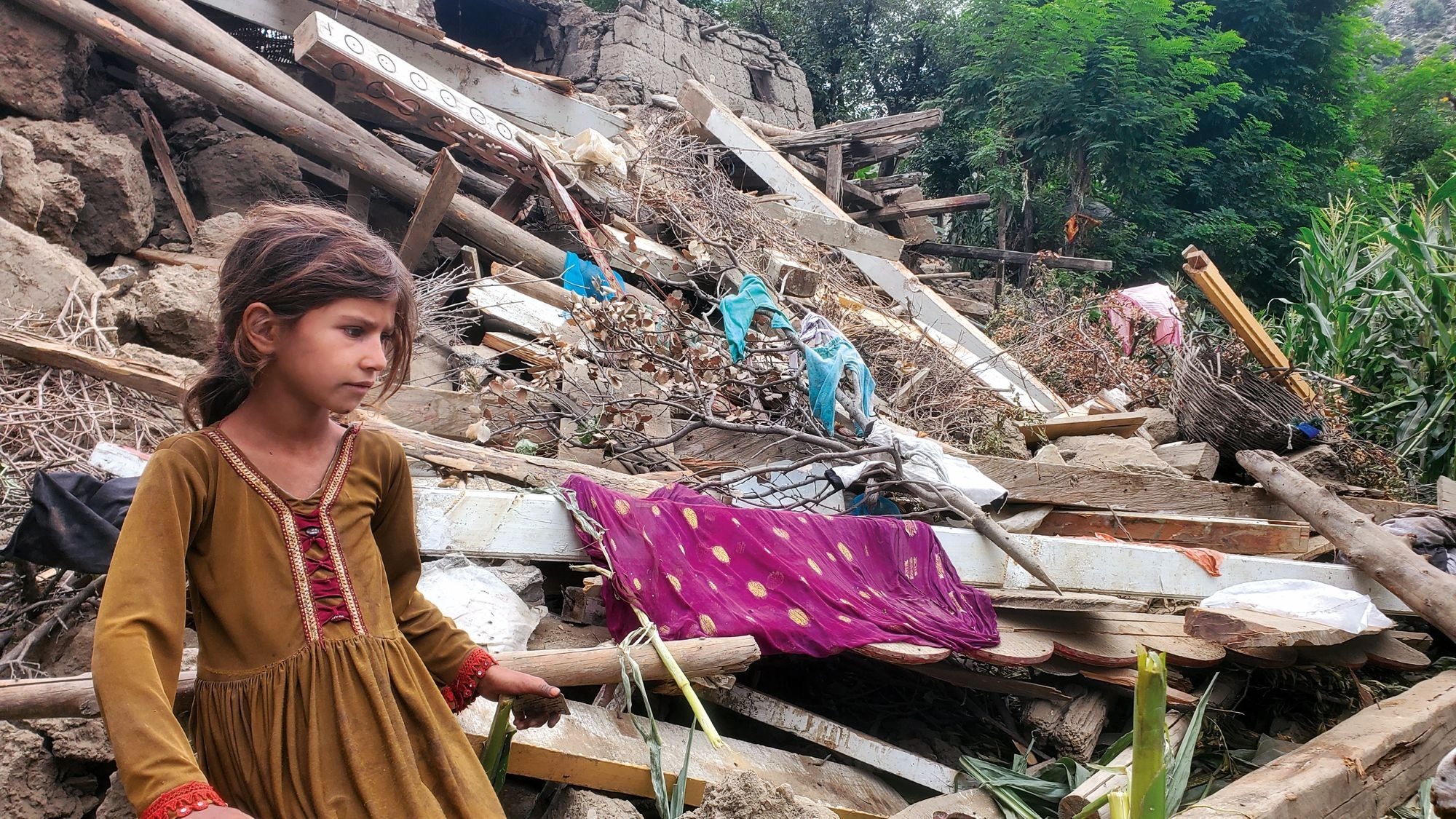 A young girl stands in front of a destroyed house in the aftermath of the earthquake