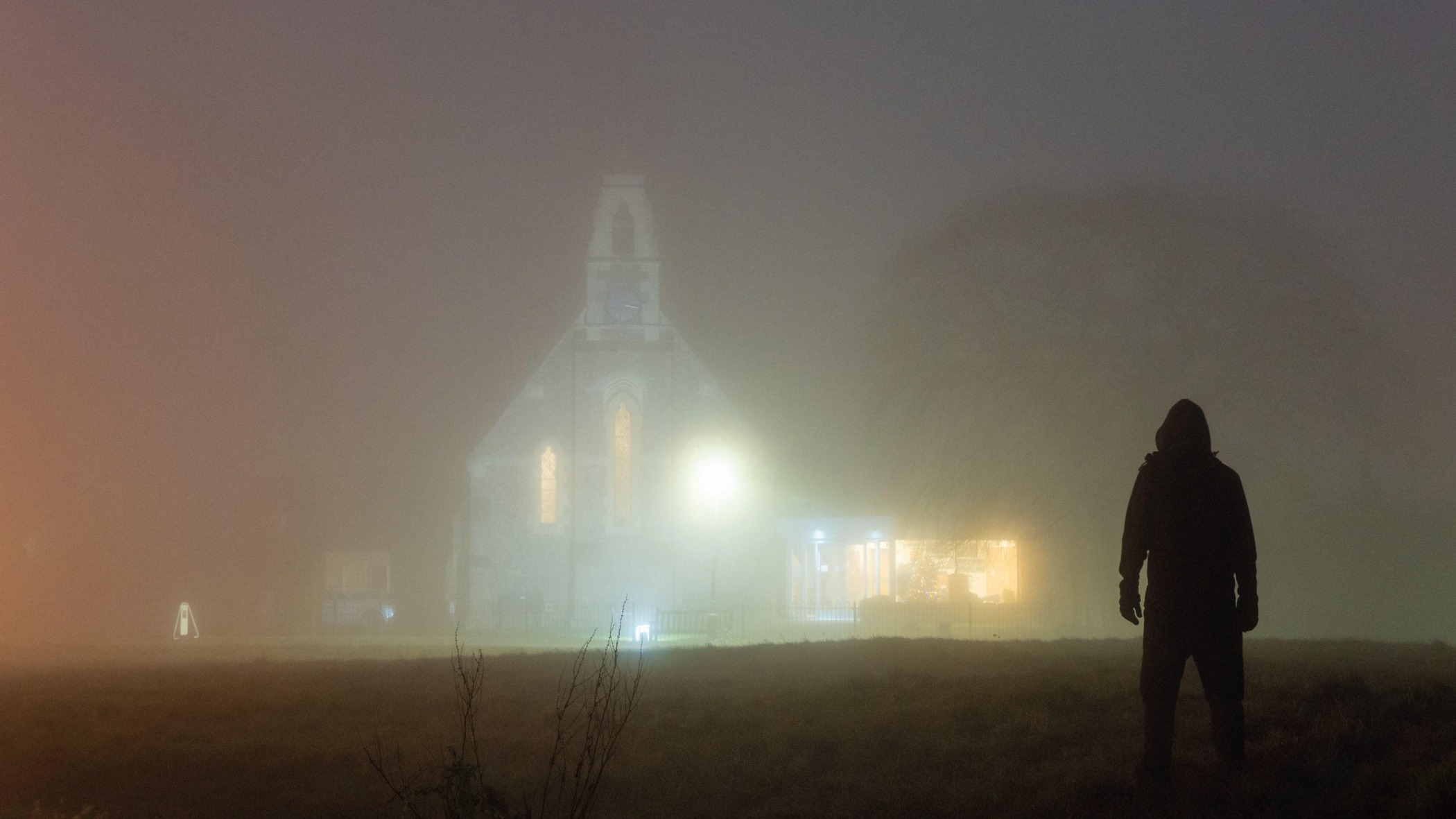 A man whose face cannot be seen stands outside a church in the dark