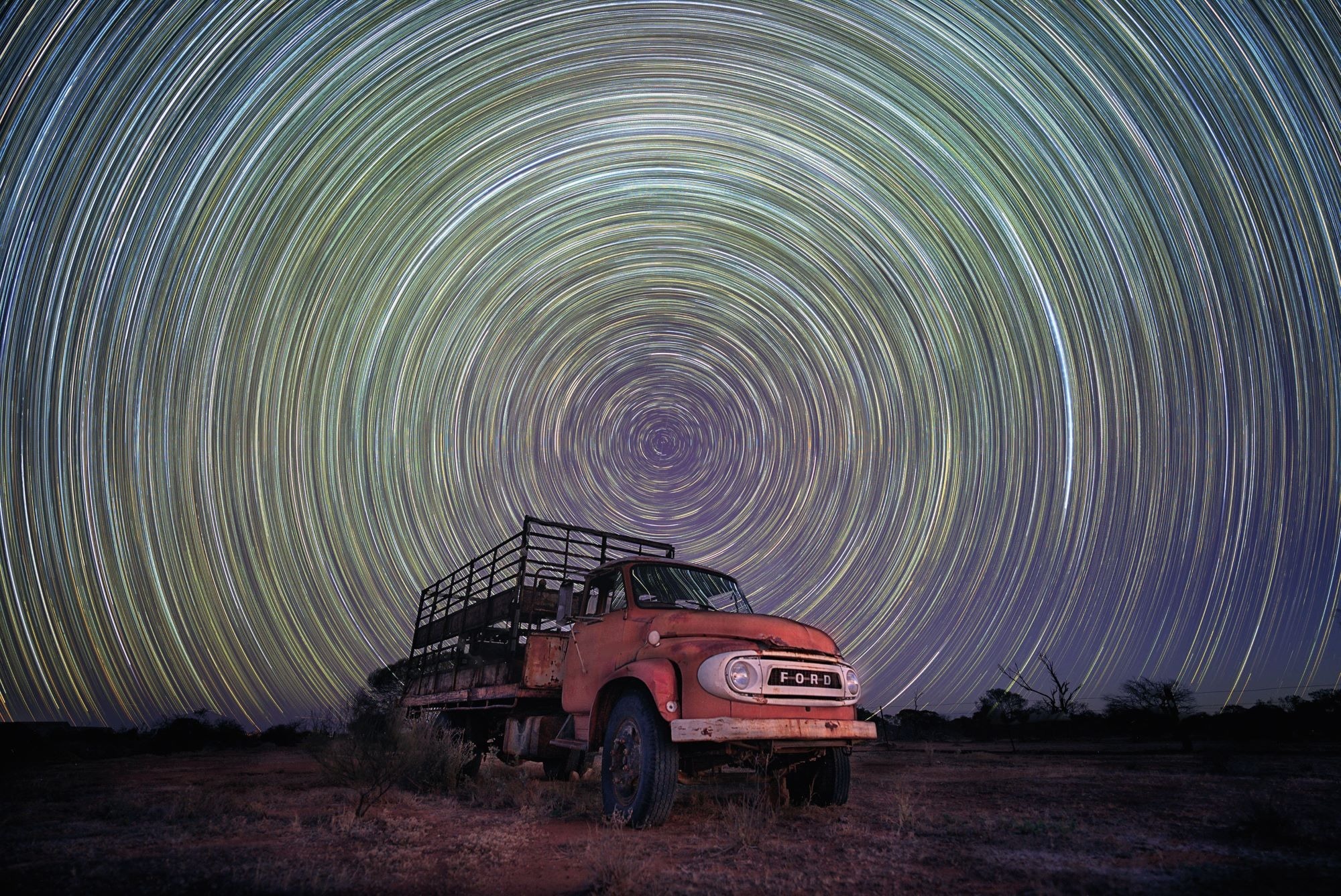 Star trails from the Earth’s rotation, captured using long exposure, appear as a series of tightly-spun glowing circles above a cattle truck in the Western Australian Wheatbelt