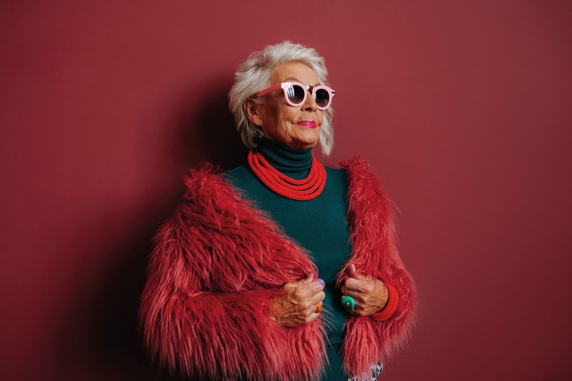 An older lady looks bold wearing a fluffy red jacket and big sunglasses