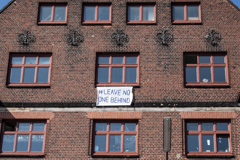 A banner hangs on the side of a building bearing the message: 'Leave no-one behind'