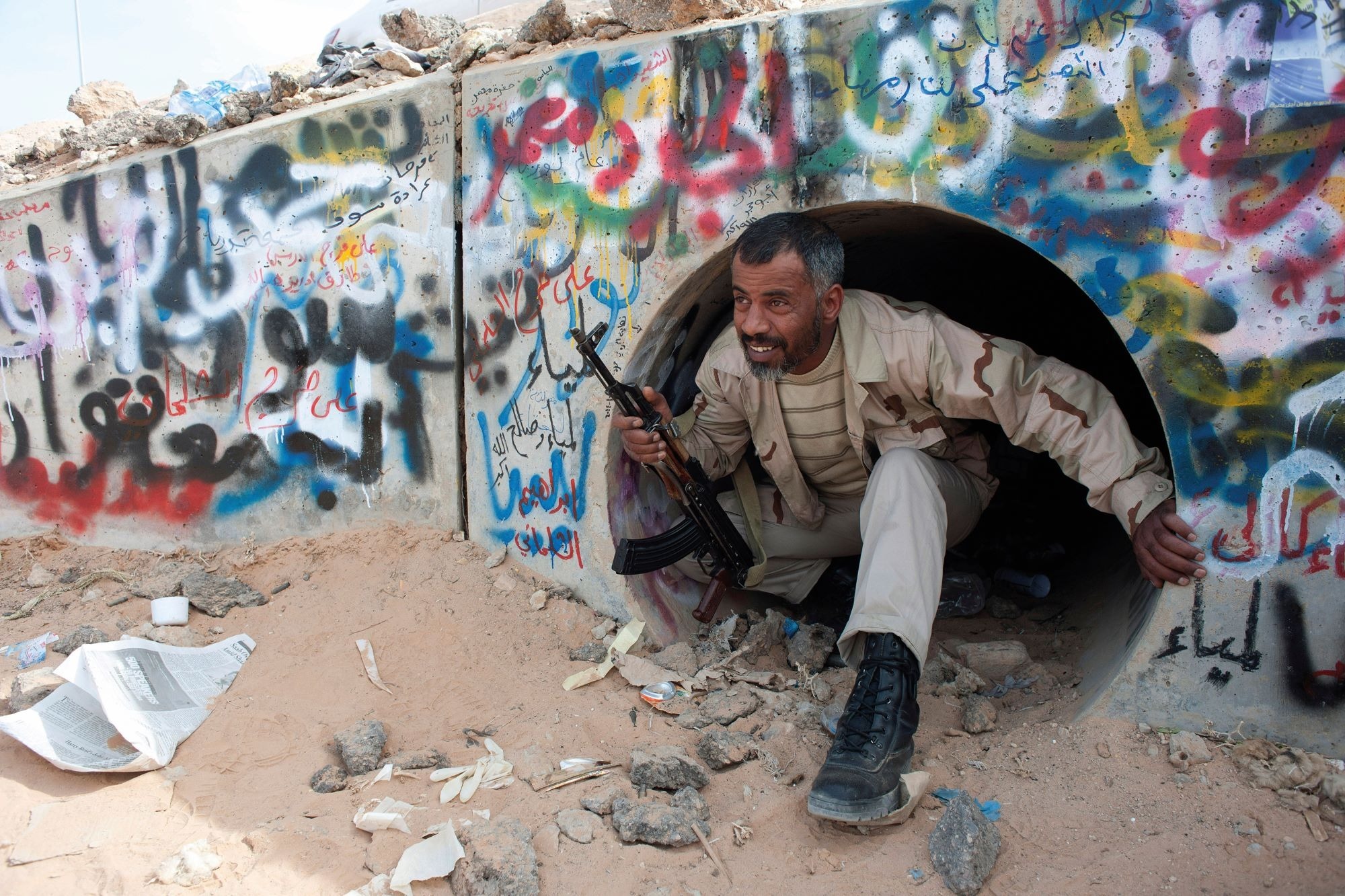 A Libyan rebel crouches down inside a graffiti-covered concrete tunnel as he demonstrates how they found Gaddafi hiding inside