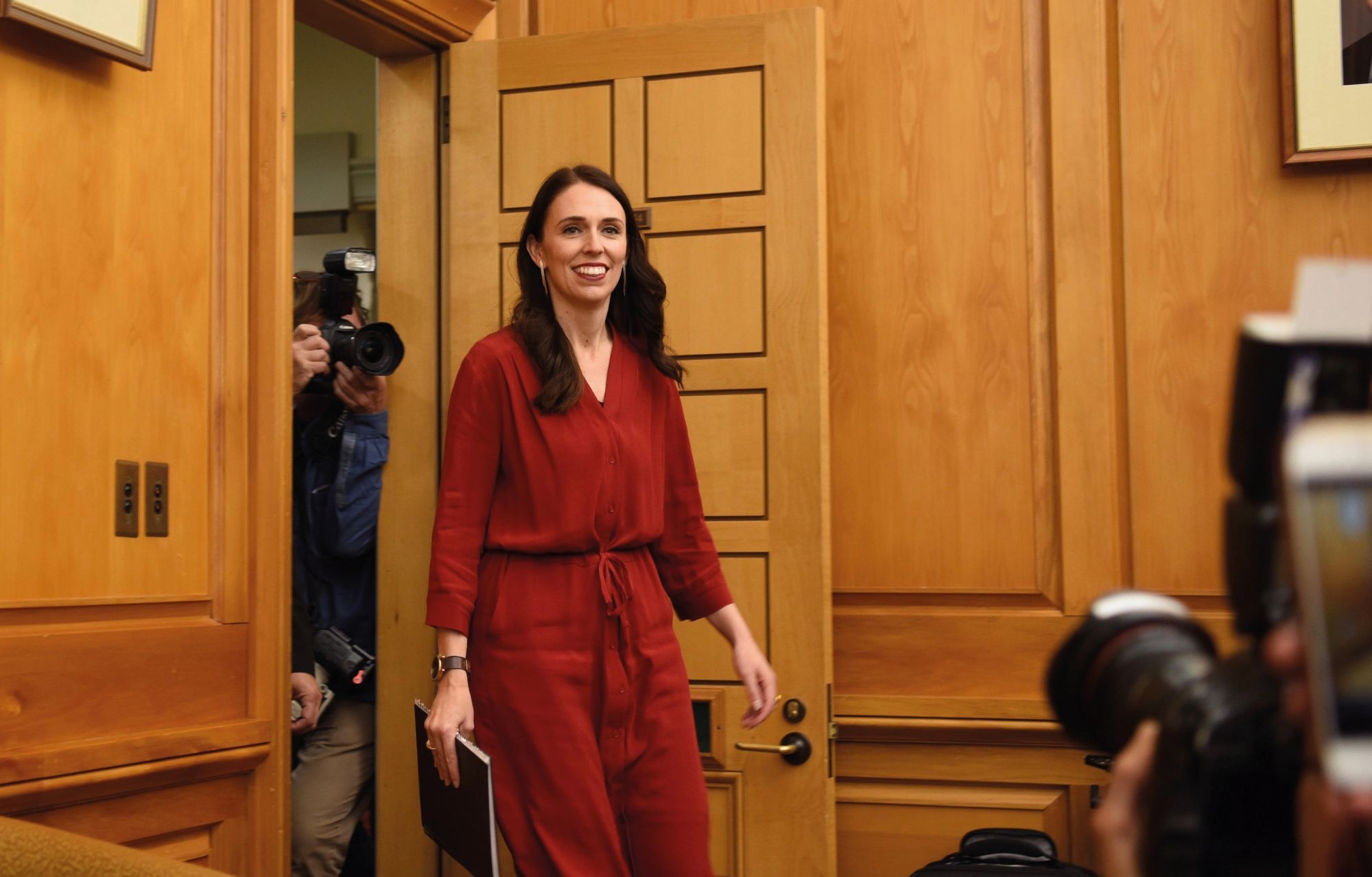 Jacinda Ardern enters a room followed by photographers