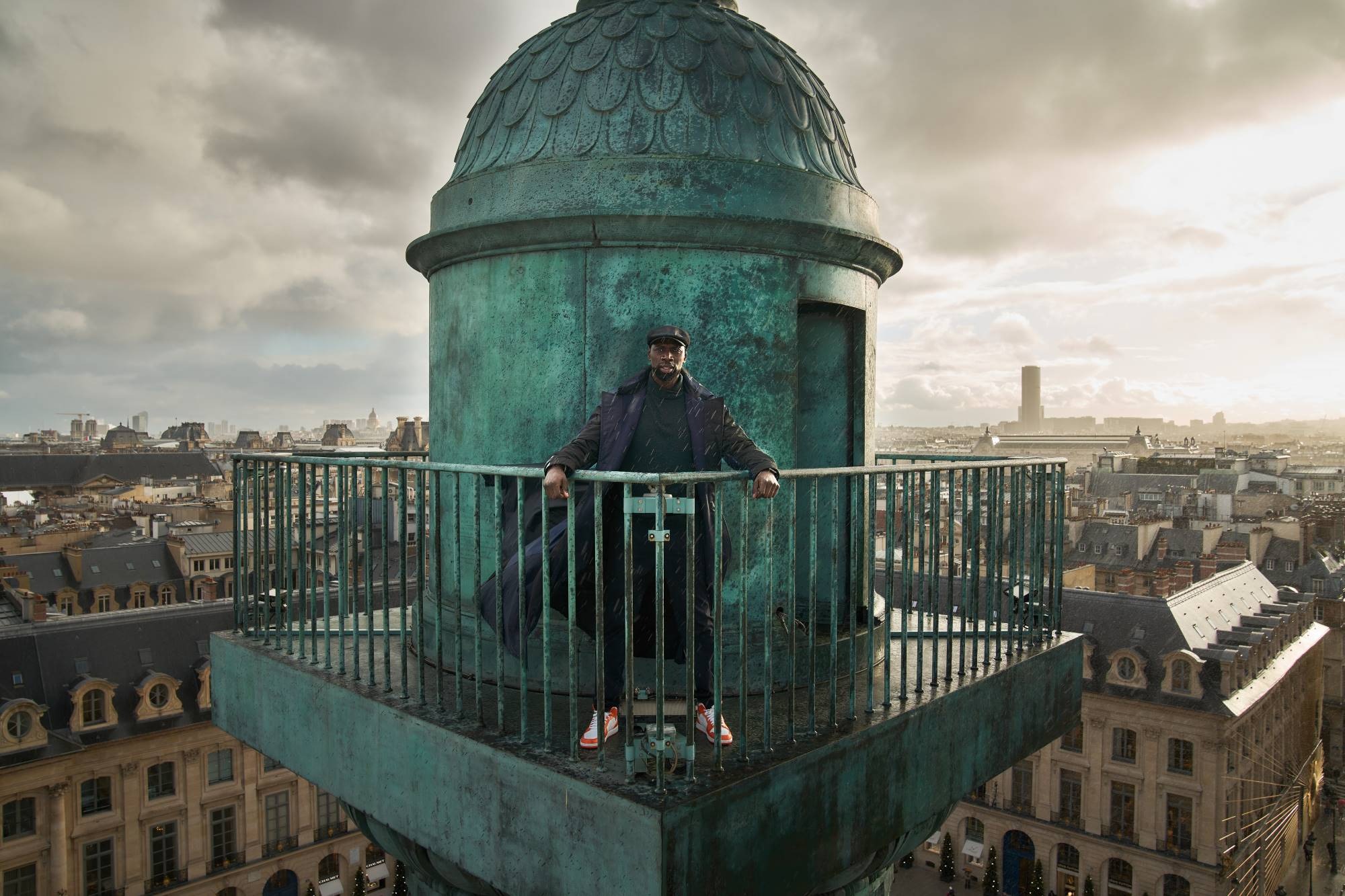 Actor Omar Sy stands on top of a tower overlooking the Paris skyline in a scene from Lupin
