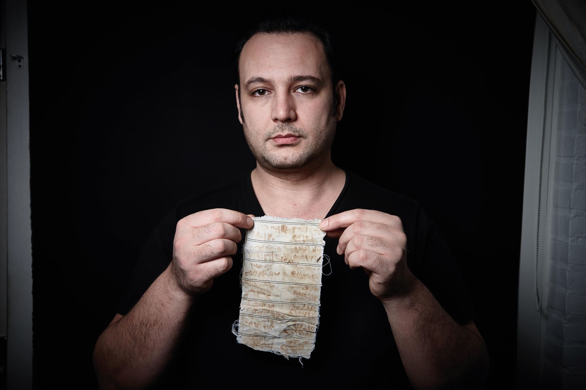 Mansour Omari holding up one of the scraps of cloth on which he wrote the names of Assad regime prisoners