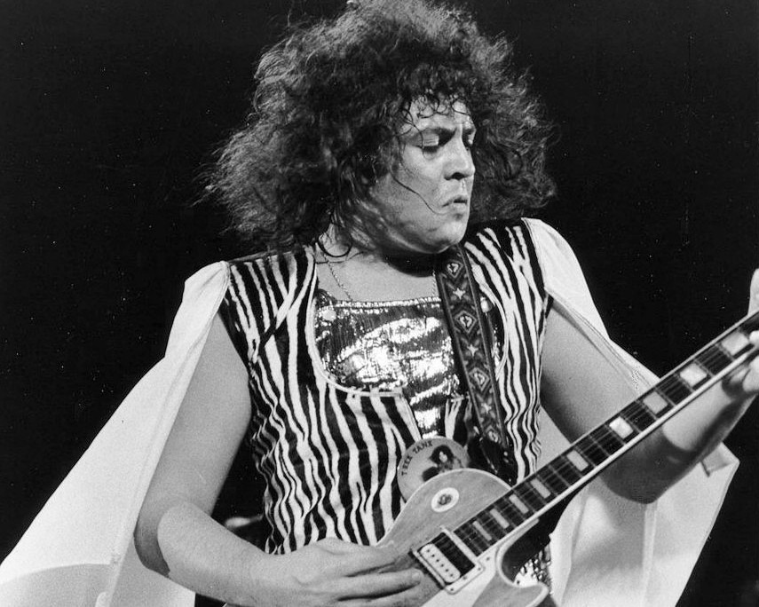 A black and white photo of Bolan playing guitar on stage in the 1970s