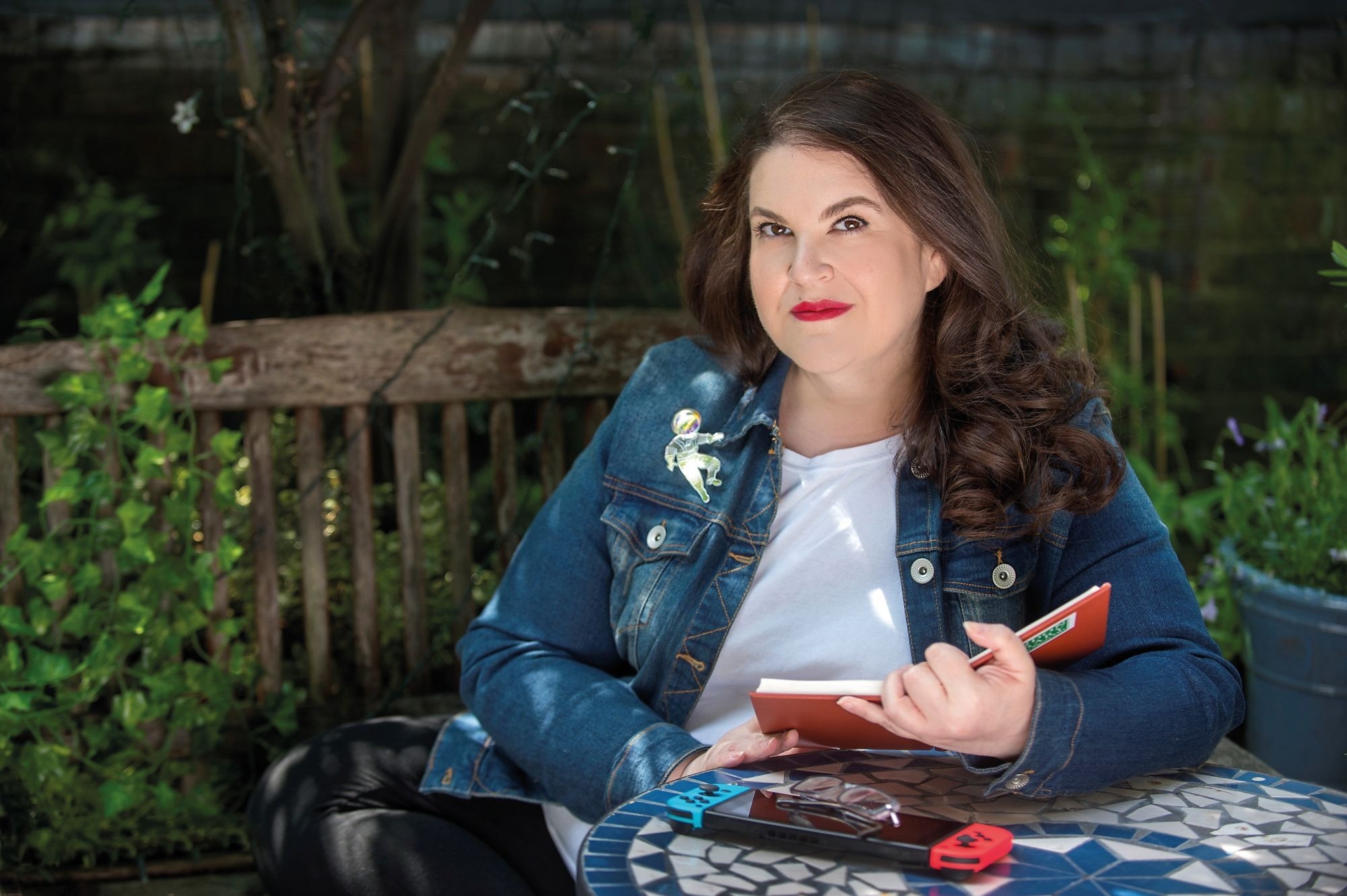 A photo portrait of Naomi Alderman sitting in a garden and reading a book
