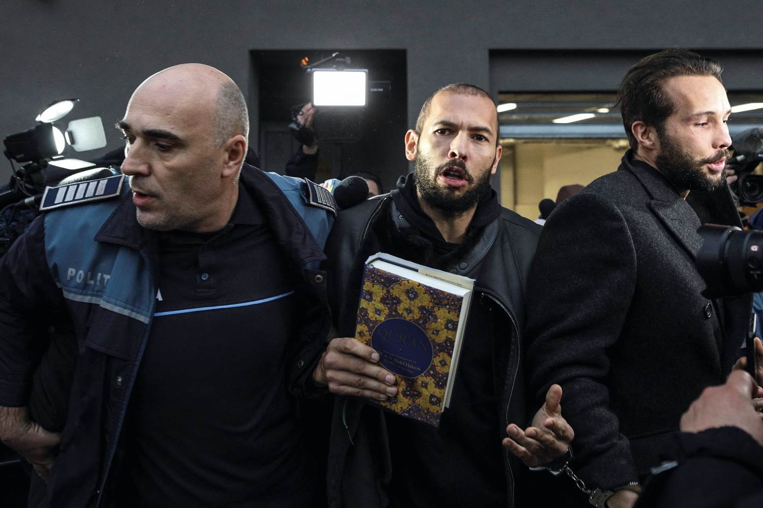 Andrew Tate carries a copy of the Koran as he is escorted by police
