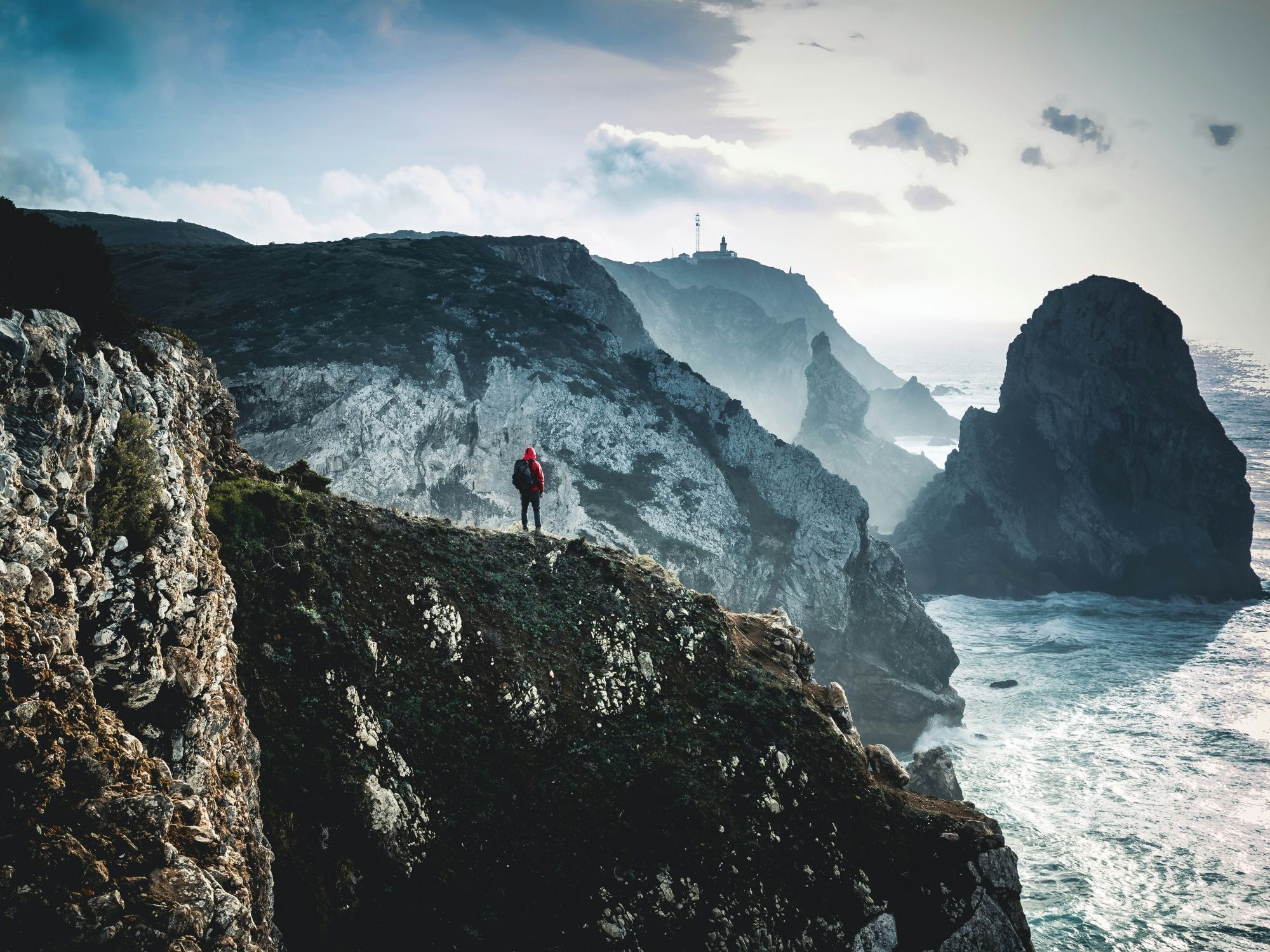 A man stands on a clifftop, surveying the vast sea and landscape in front of him