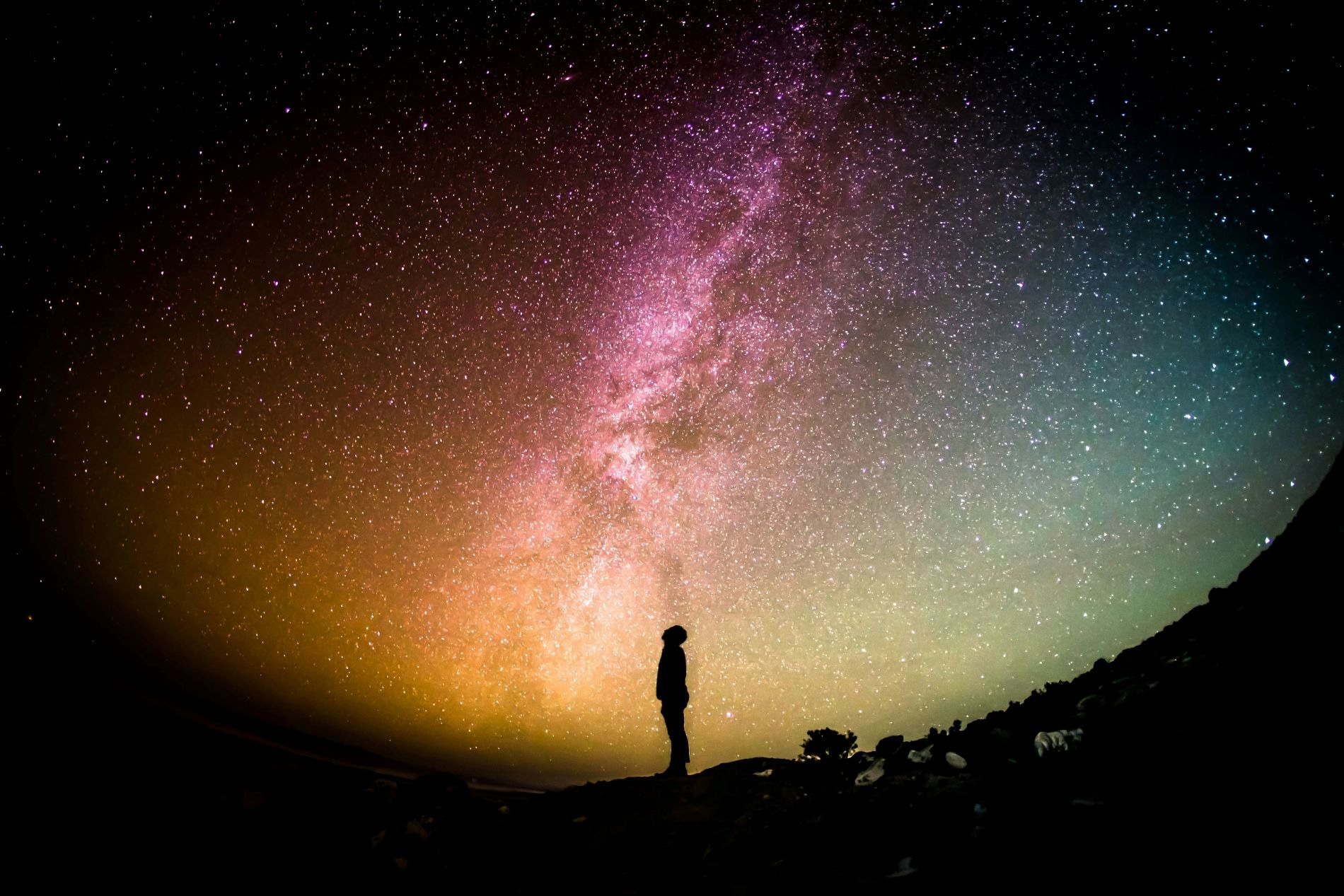 The silhouette of a person looking up in awe at a colourful night sky
