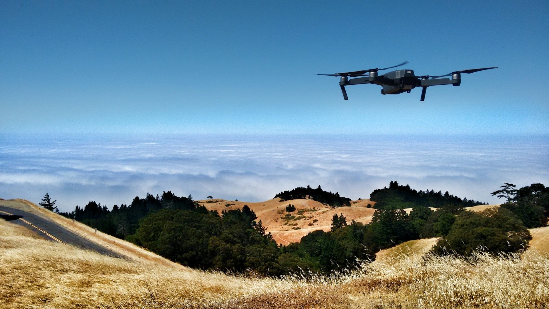 A drone used for photography hovers over a hilly landscape
