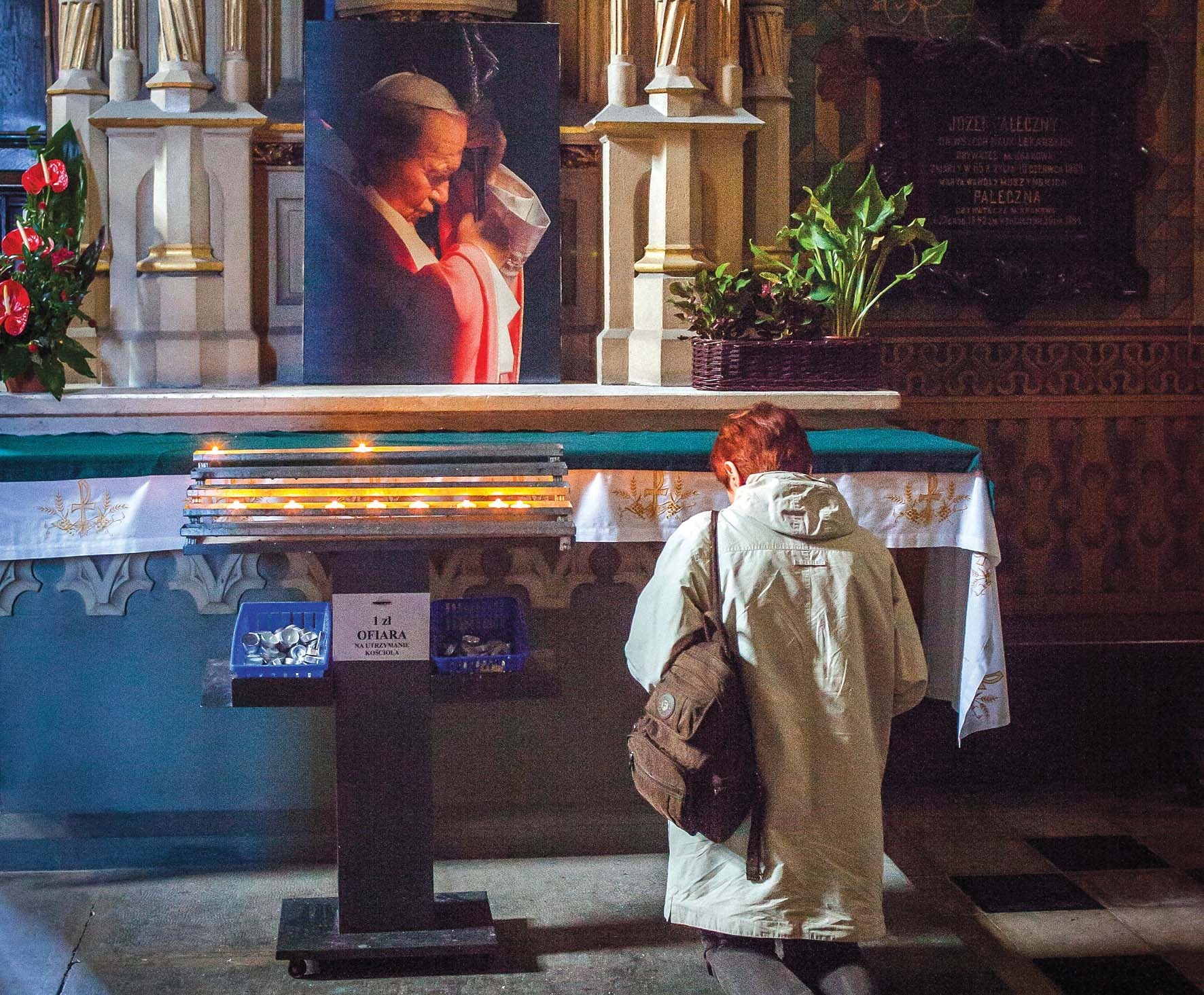 A woman praying in front of a portrait of John Paul II in Krakow, Poland
