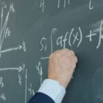 A hand writing mathematical formulas on a blackboard