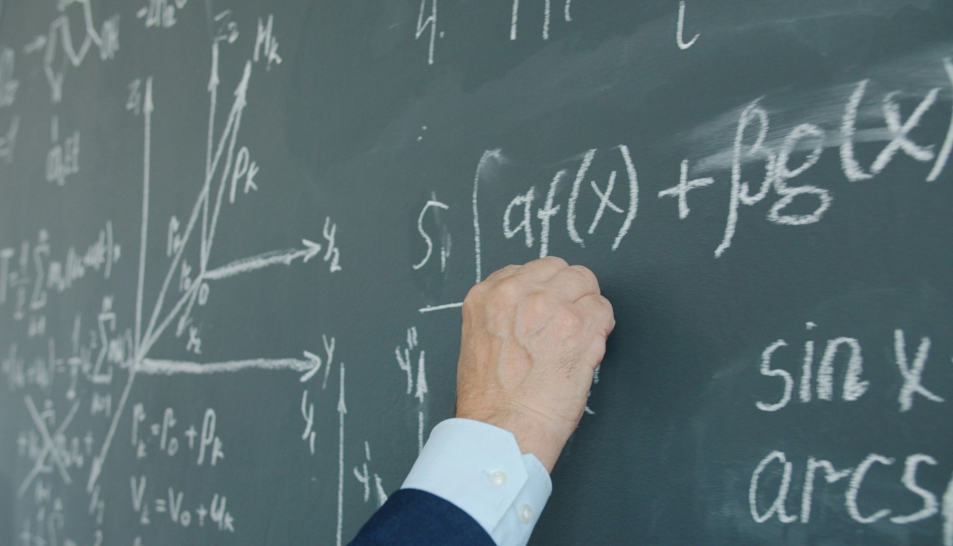 A hand writing mathematical formulas on a blackboard